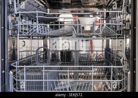 The interior of a clean, empty dishwasher showcases its multiple racks, cutlery basket, and spray arm mechanism, ready for use Stock Photo