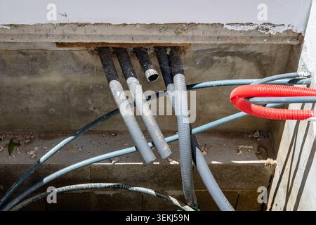 Multiple corrugated plastic conduits and flexible tubes are visible, some entering a concrete wall, indicating electrical wiring installation Stock Photo