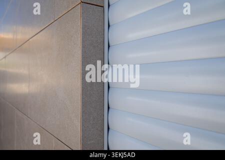 Detailed view of beige tiled exterior wall meeting a white rolling security shutter, showcasing contrasting textures and materials Stock Photo