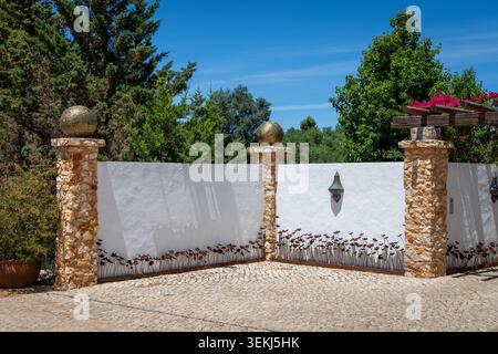 A beautiful entrance featuring textured stone pillars topped with ornate golden spheres and a white stucco wall adorned with metal poppy silhouettes a Stock Photo
