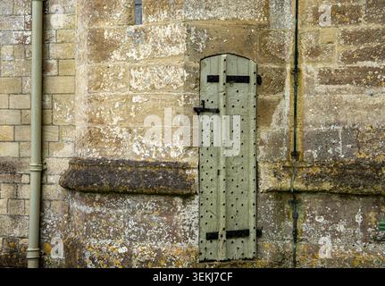 A narrow weathered wooden door with metal studs on an ancient stone church wall with textured masonry Long Newton Church Gloucestershire Stock Photo