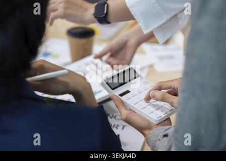 Businesswoman using a calculator to calculate numbers on a company's financial documents, she is analyzing historical financial data to plan how to gr Stock Photo