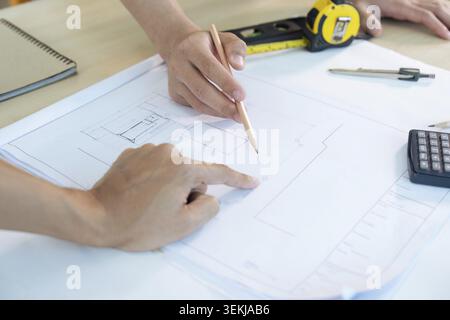 Close up of civil male engineer asian working on blueprint architectural project at construction site at desk in office Stock Photo