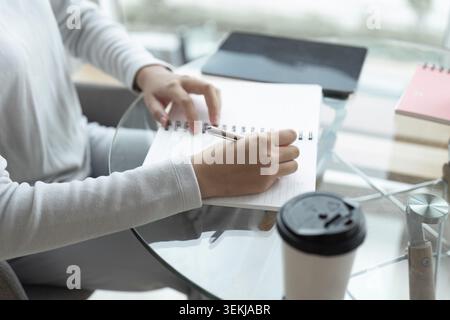 Write daily list before start each day. hands of businesswoman writing in her notebook while working at desk Stock Photo