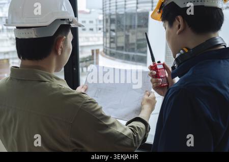 Civil engineers and architects inspecting and working building site with blueprints and holding walkie talkie Stock Photo