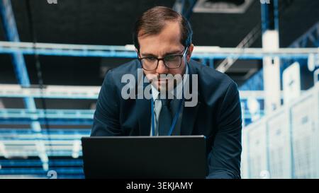 Data center admin typing on laptop keyboard, doing resource optimization using software. Server farm IT specialist using notebook program to upgrade hardware supercomputers, camera B Stock Photo