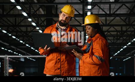 Professional engineers team coordinating production line in large-scale factory, warehouse interior features heavy equipment and modern infrastructure for massive manufacturing process. Stock Photo