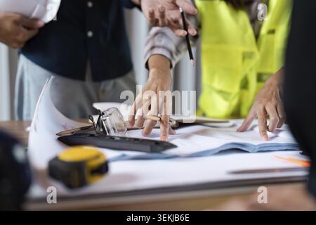 Engineers discussing project plans at a construction site, focusing on blueprints and tools, showcasing teamwork and precision Stock Photo