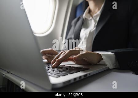 Businesswoman flying and working in an airplane in first class, sitting inside an airplane using laptop Stock Photo