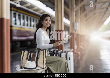 Young woman female traveler looking on map while waiting for the train at train station Stock Photo