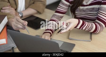 Two university students engaged in a collaborative effort, utilizing a laptop and notebook to enhance their academic project Stock Photo
