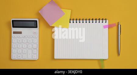 A calculator, notebook, pen, and sticky notes arranged on a yellow surface, representing organization and financial planning Stock Photo