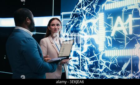Team of engineers monitors progress of artificial intelligence neural network evolution using laptop. Teamworking colleagues observing rapid development of AI machine learning tech, camera B Stock Photo