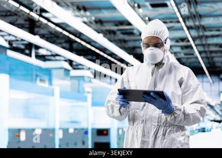 Engineer man inspecting semiconductor production infrastructure with tablet, optimizing photolithography process. Researcher trialing advanced materials for silicon wafers using device Stock Photo