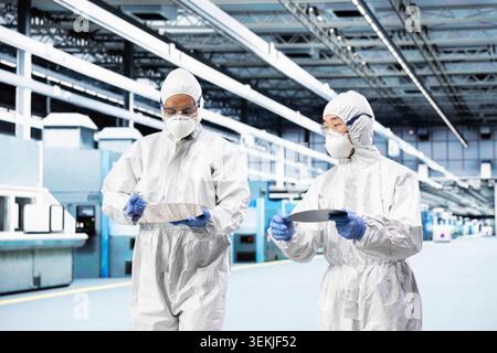 Brainstorm, silicon wafer and team of engineers doing research and development in cleanroom. Examining microelectronic defects, protective suit and teamworking colleagues with semiconductor substrate Stock Photo