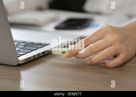 A close-up of a hand inserting a USB drive into a laptop in an office setting, illustrating the use of technology for data transfer in a business envi Stock Photo