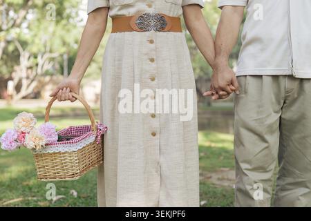 Retired couple holding hands in gardening and wife holding basket filled with flowers Stock Photo