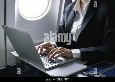 Businesswoman flying and working in an airplane in first class, sitting inside an airplane using laptop Stock Photo