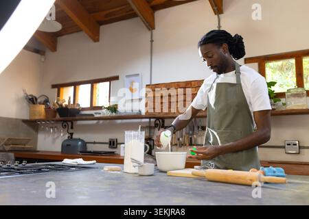 African man in green apron preparing batter on kitchen countertop with mixing bowl, copy space Stock Photo