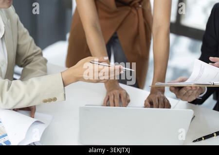 A group of professionals collaborating over documents and a laptop, emphasizing teamwork and strategy in a business meeting Stock Photo