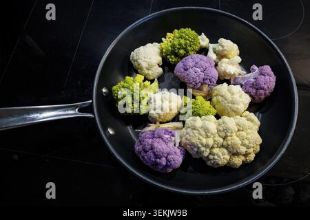 Various winter vegetables in a frying pan: white and purple florets of cauliflower (Brassica oleracea var. botrytis) and green, spiral-shaped romanesc Stock Photo