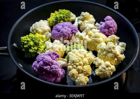 Various winter vegetables in a frying pan: white and purple florets of cauliflower (Brassica oleracea var. botrytis) and green, spiral-shaped romanesc Stock Photo