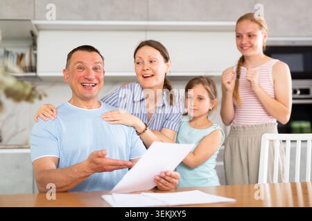 Happy satisfied family reading documents together while sitting at table at home Stock Photo