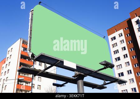 Large green billboard mockup beside residential buildings under blue sky. Advertising background outdoor marketing promotion branding and copy space. Stock Photo
