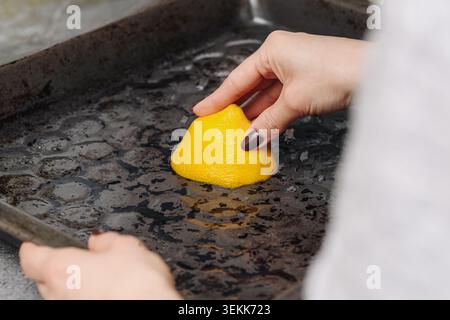 Cleaning dirty baking tray with lemon and citric acid. Natural household cleaning background promoting eco friendly home maintenance solutions. Stock Photo