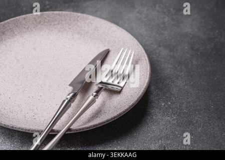 An empty round ceramic plate, knife, and fork as a dining table setting. An empty plate as a backdrop for your design Stock Photo