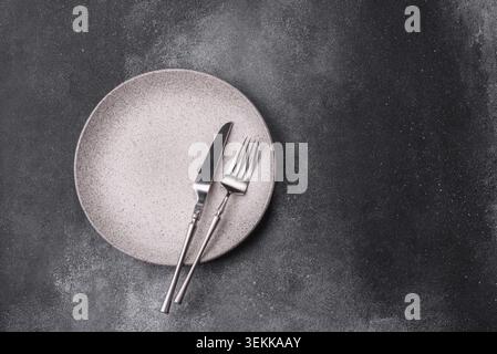 An empty round ceramic plate, knife, and fork as a dining table setting. An empty plate as a backdrop for your design Stock Photo