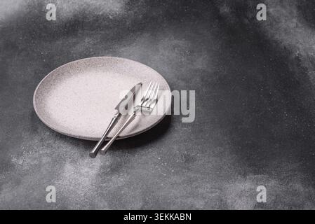 An empty round ceramic plate, knife, and fork as a dining table setting. An empty plate as a backdrop for your design Stock Photo
