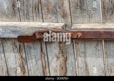 close-up shot of an old rusty metal lock mechanism mounted on a textured gray wooden plank door of a farm building Stock Photo