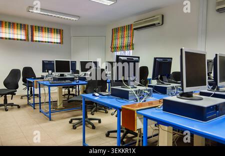 Multiple rows of desktop computer monitors and towers arranged on bright blue desks with office chairs inside an empty training center or educational Stock Photo