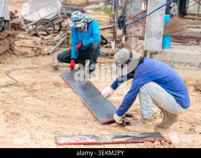 Builders crouching on dirt ground measuring and marking materials with a string line on an active industrial building construction site. Stock Photo