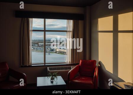 inside view of a room with two red chairs and a small table next to a window and the morning light on the wall Stock Photo
