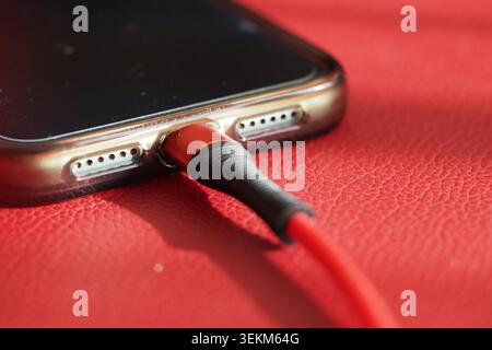 Charging a smartphone with a red cable on a red surface Stock Photo