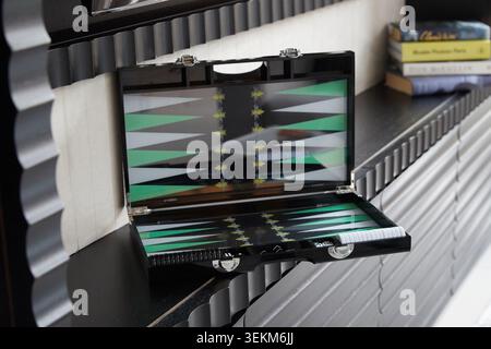 Open luxury black and green backgammon board displayed on an interior shelf with books and contemporary decor in the background. Stock Photo