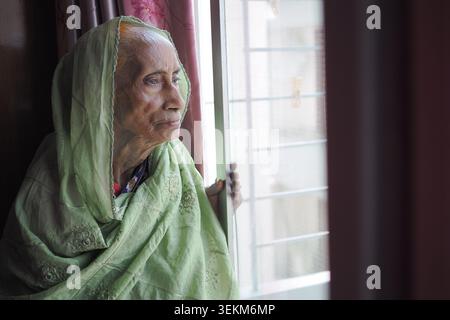 Elderly woman looking out of window in a home setting Stock Photo