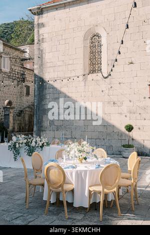 Elegant outdoor dining table set in a sunlit stone courtyard beside an old wall Stock Photo