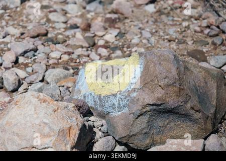NASU, TOCHIGI, JAPAN - APRIL 12, 2026: A yellow and white trail marking is painted on a volcanic rock alongside the mountain path on Nasu, Tochigi, Japan. The vivid color contrast against the brown rocky ground guides hikers safely along the volcanic mountain route. Stock Photo
