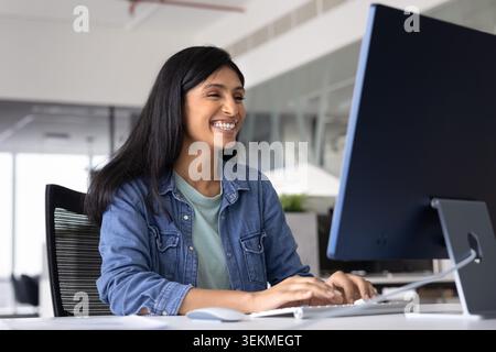 Happy Indian office employee working on computer in modern office Stock Photo