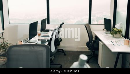 Row, workstation and desk with computer in office, programming department and setup in digital agency. Empty, interior and desktop by window at tech Stock Photo