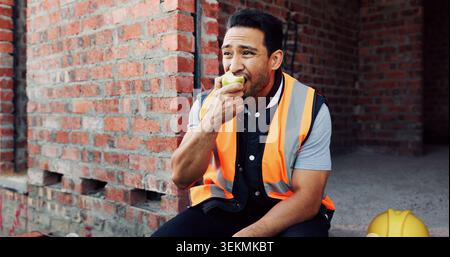 Man, architect and eating with apple on construction site for lunch break, rest or meal. Hungry contractor, male person or civil engineer with natural Stock Photo