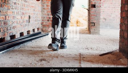 Walking, building and feet of person on construction site for planning, infrastructure and inspection. Architecture, civil engineer and legs of worker Stock Photo