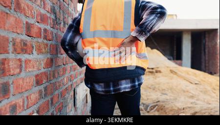 Person, architect or hands with back pain on construction site for overworked, strain or incident. Contractor, civil engineer or discomfort with sore Stock Photo
