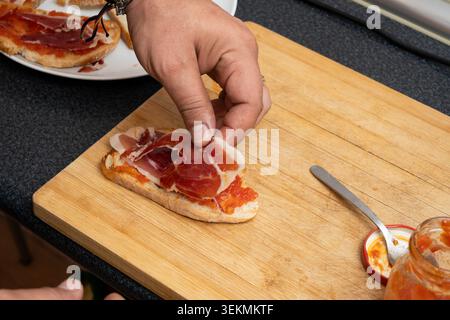 Hand placing cured ham slices on toast with tomato spread Stock Photo