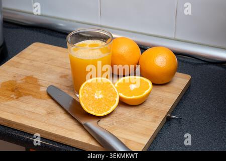 Freshly squeezed orange juice, whole oranges, and cut oranges on a wooden cutting board Stock Photo