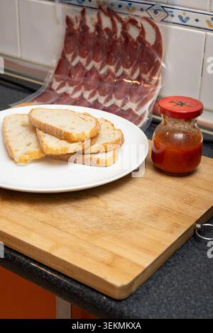 Preparing a snack with bread, tomato sauce, and Spanish ham on a cutting board Stock Photo