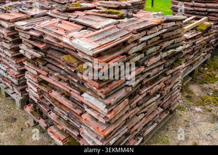 Stack of reclaimed clay roof tiles stored on pallets for recycling and building restoration work Stock Photo